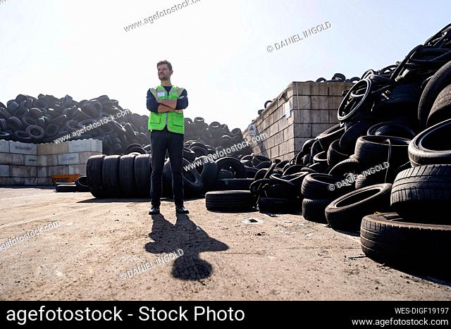 Man with arms crossed standing by tires at recycling plant