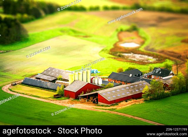 Rural farm in red colors with green fields around in the agriculture industry seen from above