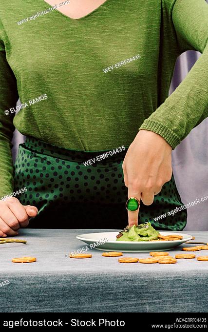 Close-up of woman with finger in guacamole on table at home