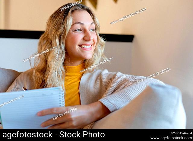 Happy caucasian woman sitting on sofa in living room, taking notes