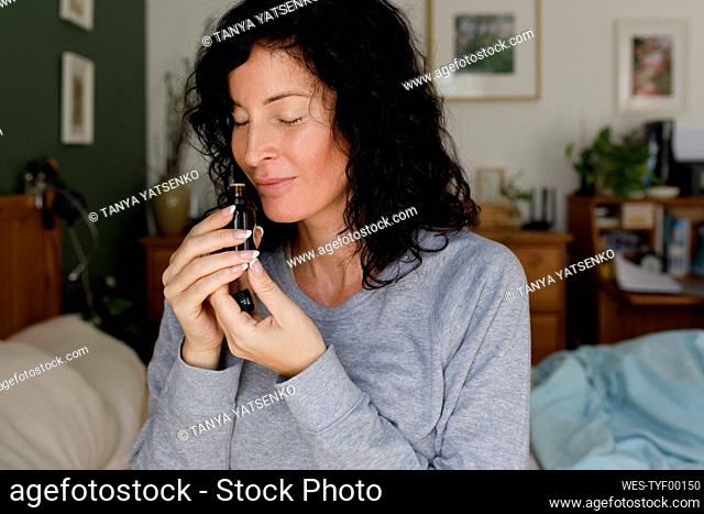 Woman with eyes closed smelling essential oil from bottle at home