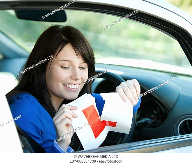 Brunette teen girl sitting in her car tearing a L-sign after having her drivers licence