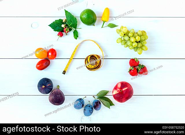 Fitness healthy food on white wooden background (lime, strawberry, plum, figs, raspberries, grapes, peppers, peaches, tomatoes nectarines and measuring tape)