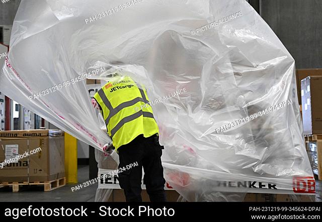 PRODUCTION - 07 December 2023, Hesse, Frankfurt/Main: A DB Schenker Jetcargo employee throws a film over a pallet of freight in the logistics company's air...