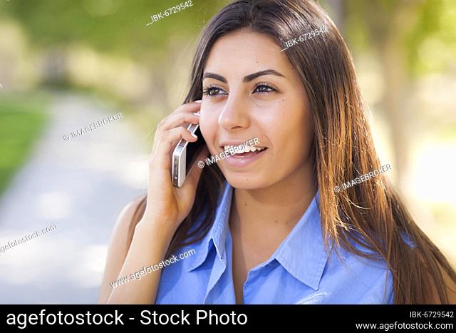 Smiling mixed-race young adult woman using her cell phone outside