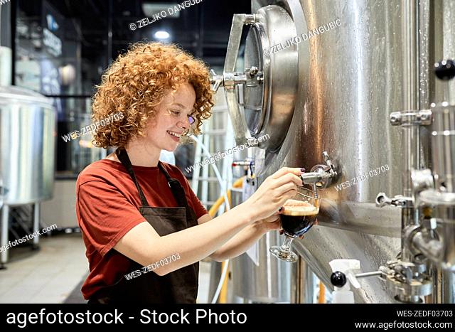 Woman working in craft brewery tapping beer from tank