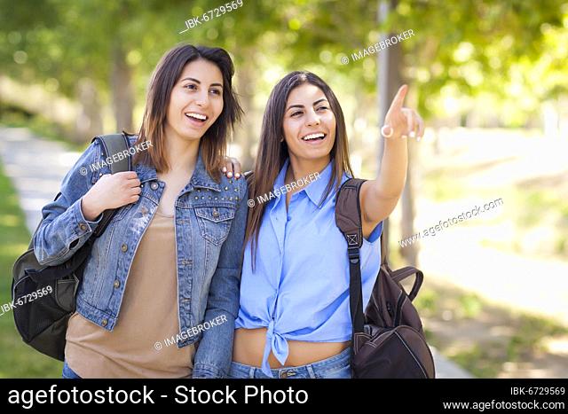 Young adult mixed-race twin sisters wearing backpacks and pointing outside