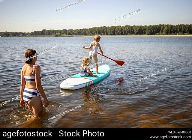 Girls having fun on paddleboard with mother at lake