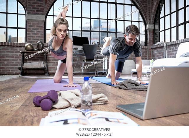 Young man and woman with laptop doing yoga exercise