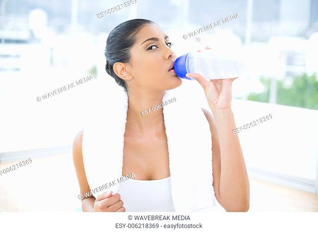 Calm toned brunette with towel drinking from sports bottle