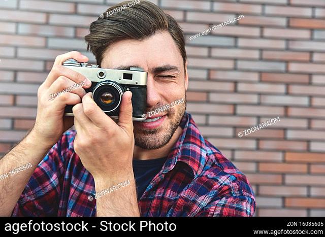 Man with retro photo camera Fashion Travel Lifestyle outdoor while standing against brick wall background