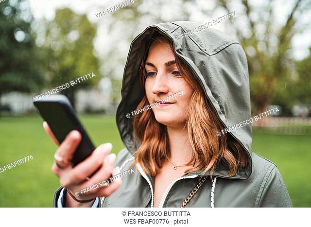 Young woman wearing hooded jacket and using cell phone on a rainy day