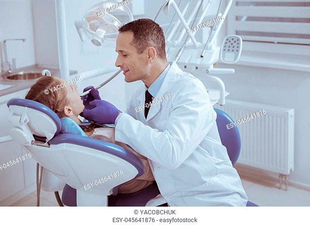 Dental checkup. Happy male male dentist using dental instrument while examining patients teeth