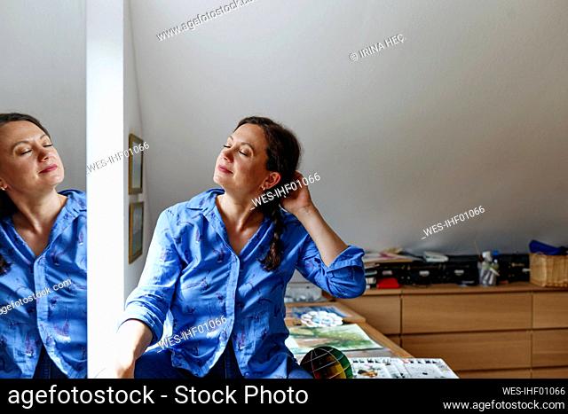 Woman with eyes closed and hand in hair sitting on table at home