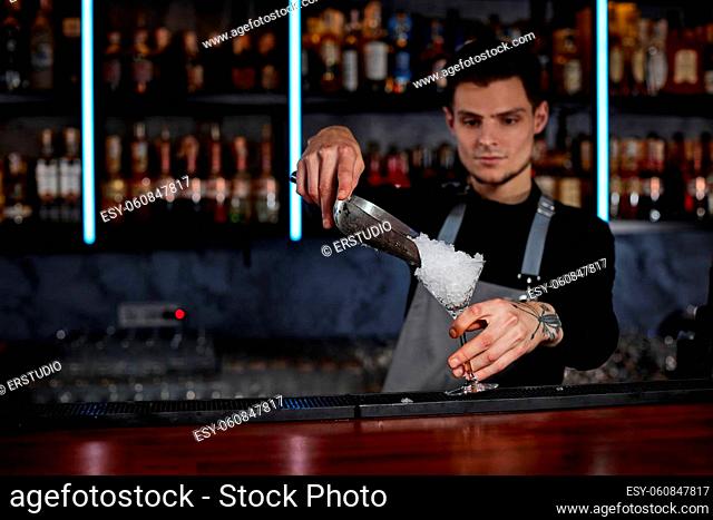 Barman puts the ice cubes into alcoholic drink glass at the bar