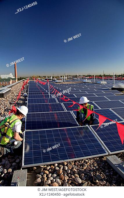 Denver, Colorado - Workers install solar photovoltaic panels on the roof of Harrington Elementary School  The worker inside the red-flagged zone wears a fall...