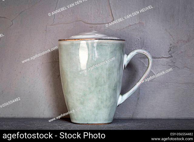 Ceramic mug with white foam gray natural stone design with concrete wall background, coffee or tea concept, copy space close up