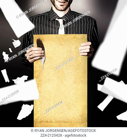 Male writer holding old quill and blank story scroll with falling pieces of paper. Author and novelist concept on grey studio background
