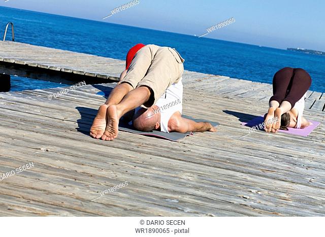 People practising yoga on boardwalk, plow pose