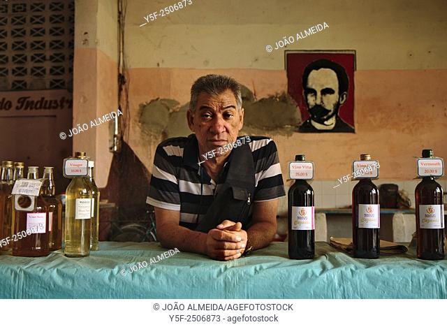 Wine seller at Cienfuegos market with an image of Jose Marti, on the heroes of Cuba independence, in the background