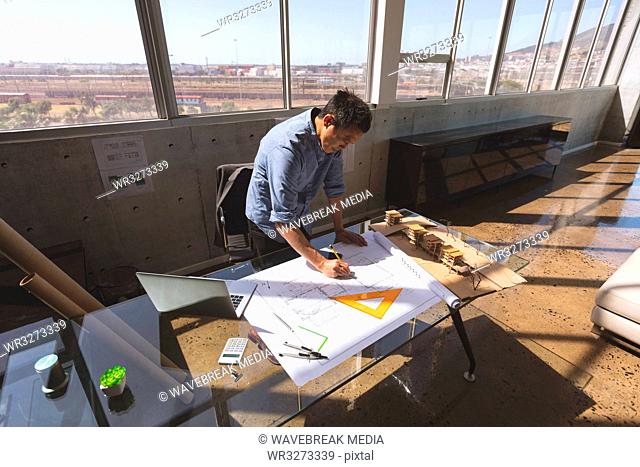 Male architect standing at desk and working on blueprint in a modern office