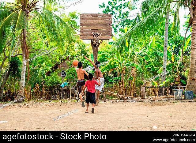 Sandugan, Siquijor, Philippines - May 13 2013: Three kids playing basketball at sand field with old wooden basketball basket