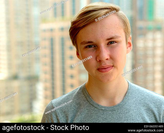 Portrait of young handsome blond teenage boy against view of the city outdoors