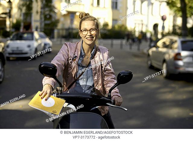 Woman on motor scooter, holding city tour guide map, in Berlin, Germany