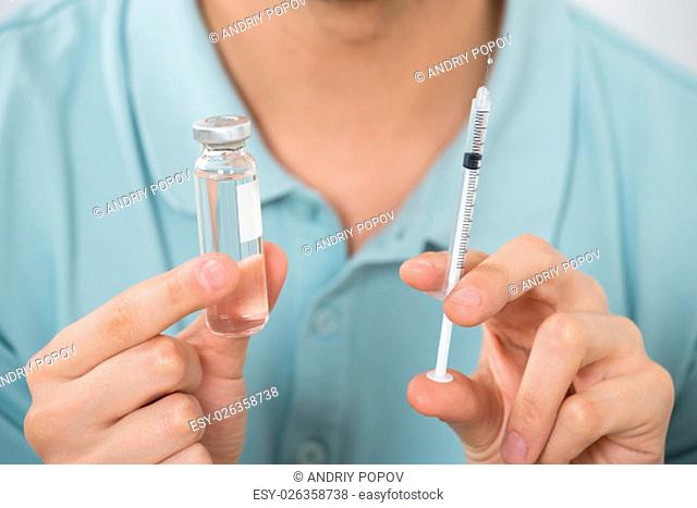 Close-up Of Young Man Holding Medicine Bottle And Syringe