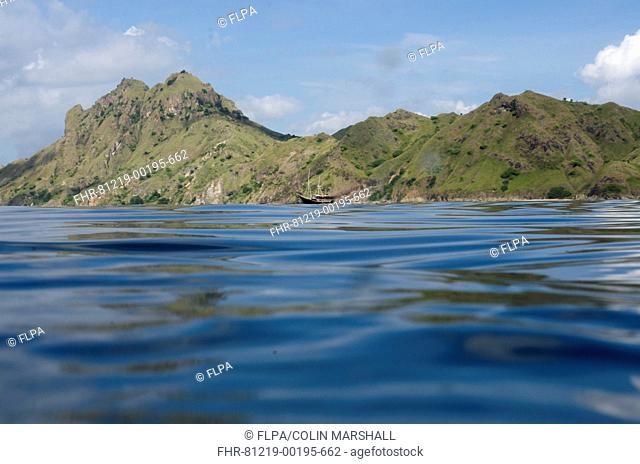 View of coastline with hills and ship from surface of sea, Mobula Point dive site, Padar Island, Komodo N.P., Lesser Sunda Islands, Indonesia, March