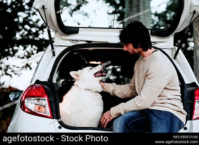 Man sitting with dog in car trunk at forest