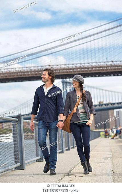Couple walking on promenade, Brooklyn Bridge in background
