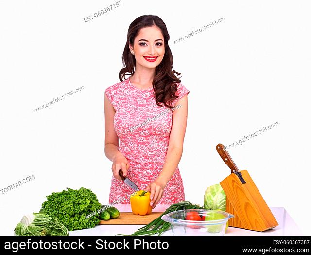 Beautiful brunette girl slices vegetables for salad sitting at the kitchen table on a isolated white background