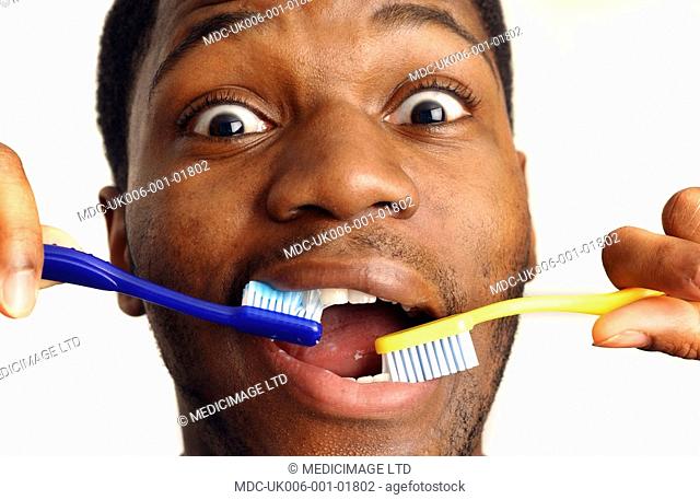 Young man brushing teeth with two toothbrushes