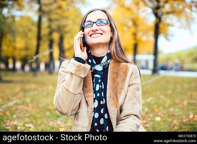 Woman sitting in the grass in fall using her phone to call a friend