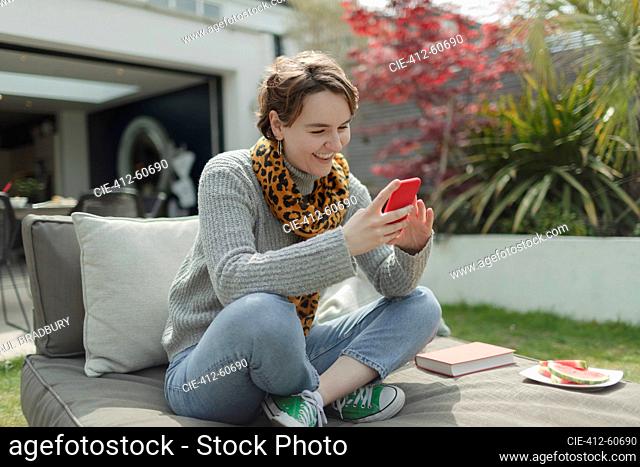 Smiling young woman using smart phone on patio lounge chair