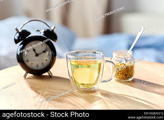 alarm clock and cup of chamomile tea on table