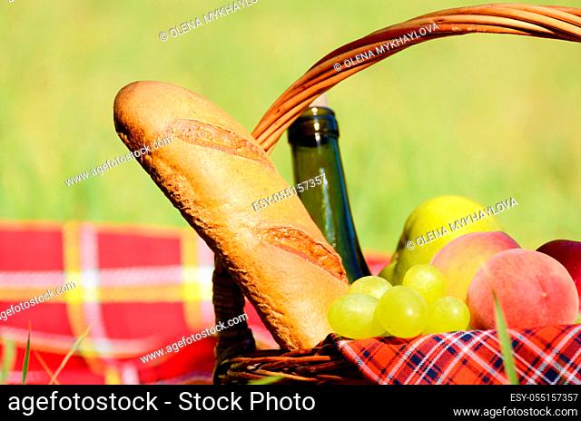 Picnic basket with red napkin fool of fruits, bread and wine on green grass