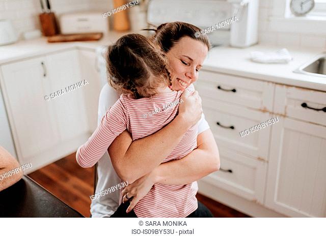 Mother hugging daughter in kitchen