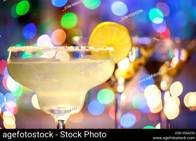 Glasses of margarita and martini cocktails on bar lights background