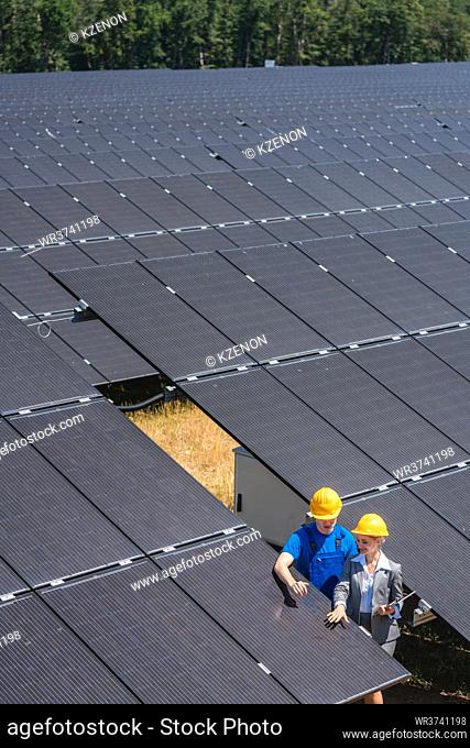 Two people standing amid solar cells in a power plant inspecting the modules
