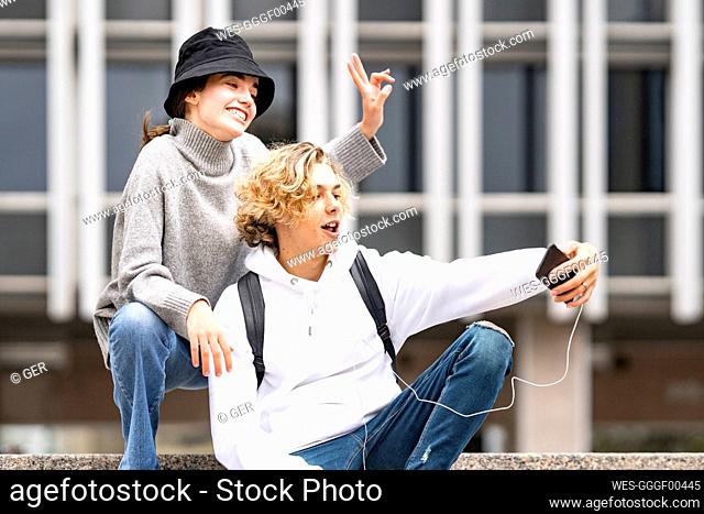 Blond man taking selfie while female friend doing peace sign