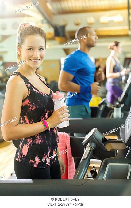 Portrait smiling woman with water bottle on treadmill at gym