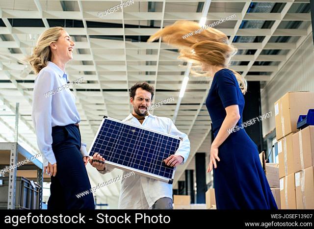 Carefree businessman playing with solar panel by colleagues at warehouse