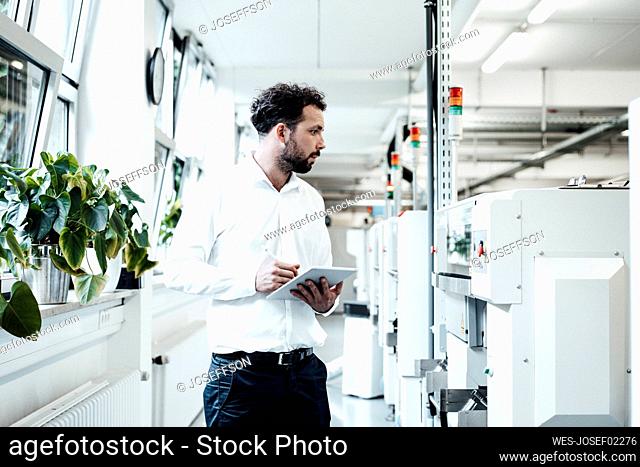 Businessman holding digital tablet while looking at machinery in bright industry