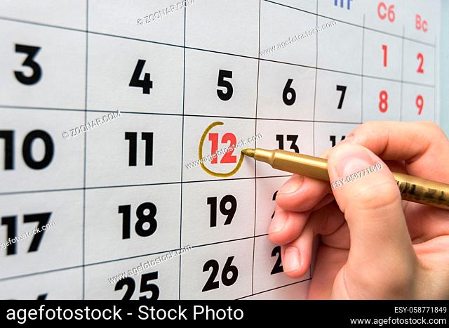 Hand with a marker on the wall calendar leads around a red holiday