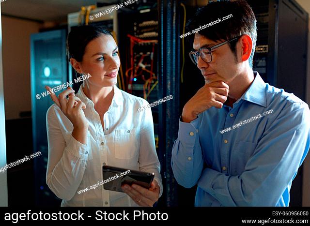 Diverse male and female engineers with digital tablet discussing in computer server room