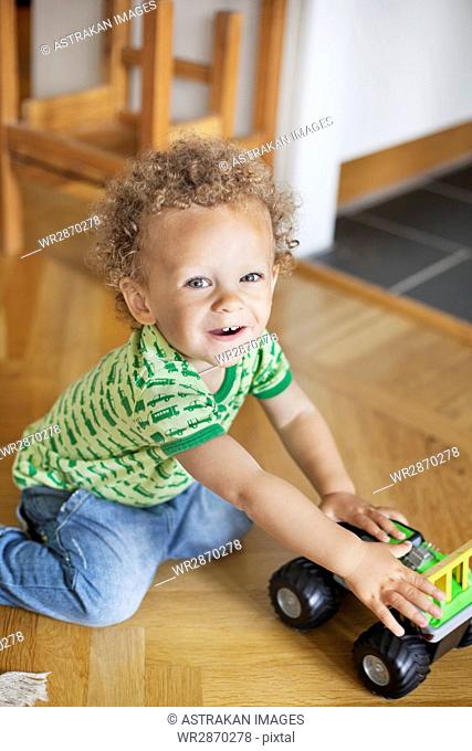 Portrait of cute boy playing with toy car on hardwood floor at home