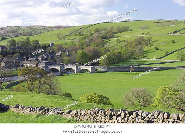 View of five arched stone bridge over River Wharfe, drystone wall, pasture, trees and village, Burnsall, Wharfedale, Yorkshire Dales N P , North Yorkshire
