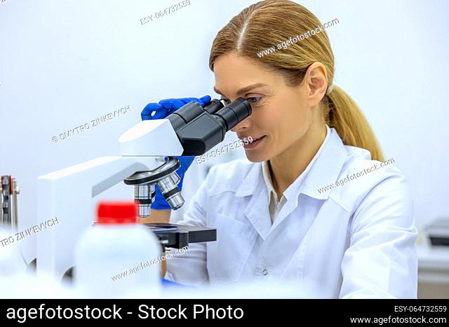 Medical female scientist looking under microscope, doing analysis of test sample, ambitious biotechnology specialist working in laboratory